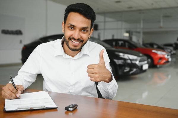 young indian man signing documents at car dealership