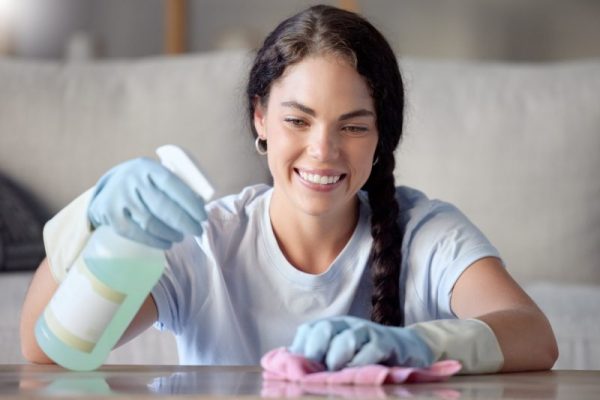 Cleaning, nanny and woman spray a table surface to remove bacteria and dirt for hygiene in a home,