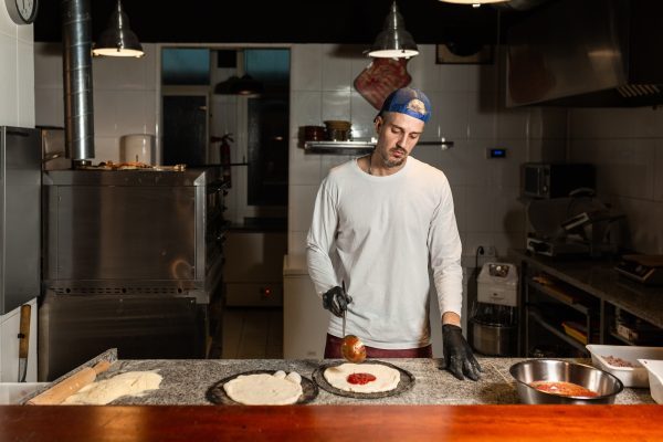 pizza man adds tomato to a pizza in a pizzeria restaurant kitchen